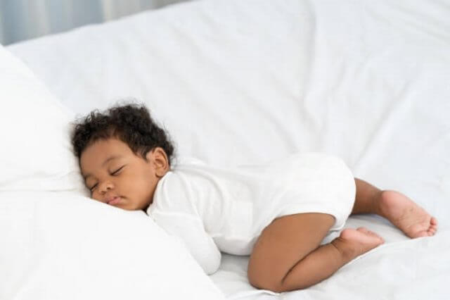 black african american baby sleeping on a white mattress.